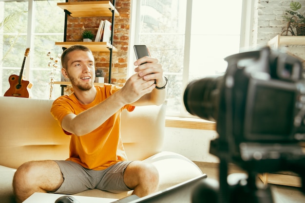 Free photo young caucasian male blogger with professional camera recording video review of smartphone at home