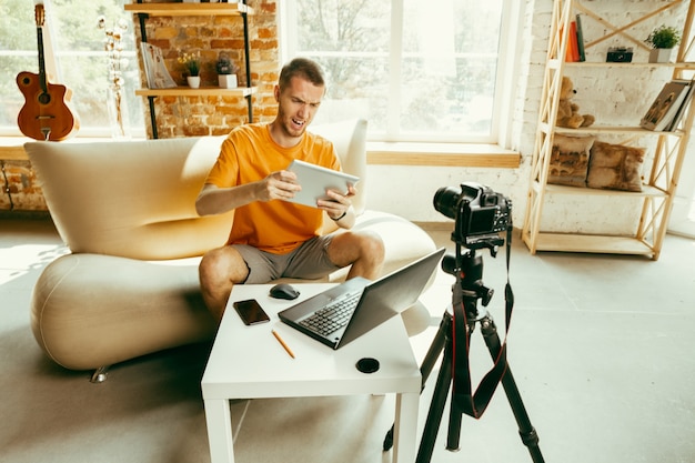 Free photo young caucasian male blogger with professional camera recording video review of tablet at home