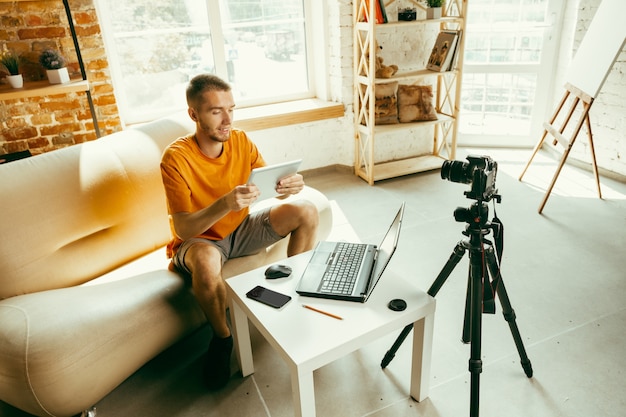 Young caucasian male blogger with professional camera recording video review of tablet at home