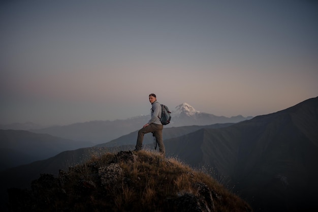 Free photo young caucasian male hiker standing at the top of a grassy mountain and admiring the foggy nature