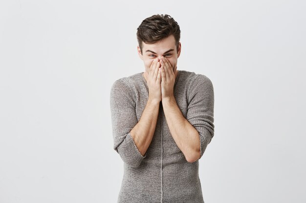 Young caucasian man having bugged eyes, covers mouth looks in terror, being emotional or scared after hearing shocking news on radio, isolated . Negative emotions