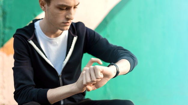 Free Photo young caucasian man is on his fitness bracelet on multicolored background