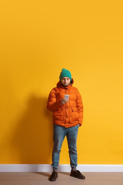 Free photo young caucasian man using smartphone full body length portrait isolated over yellow wall