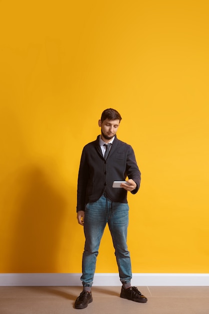 Young caucasian man using smartphone full body length portrait isolated over yellow wall