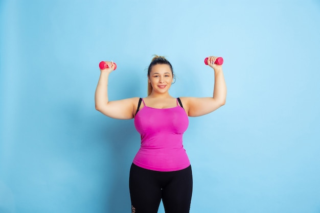 Free photo young caucasian plus size female model's training on blue background