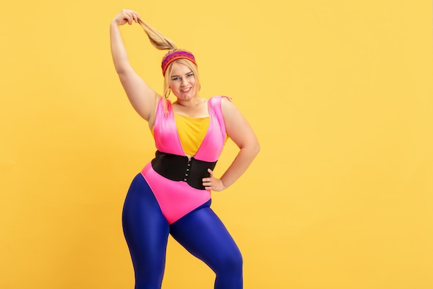 Free photo young caucasian plus size female model training on yellow