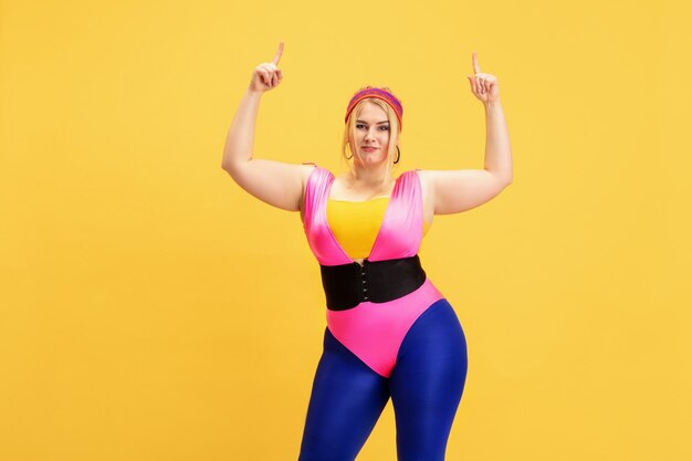 Young caucasian plus size female model training on yellow