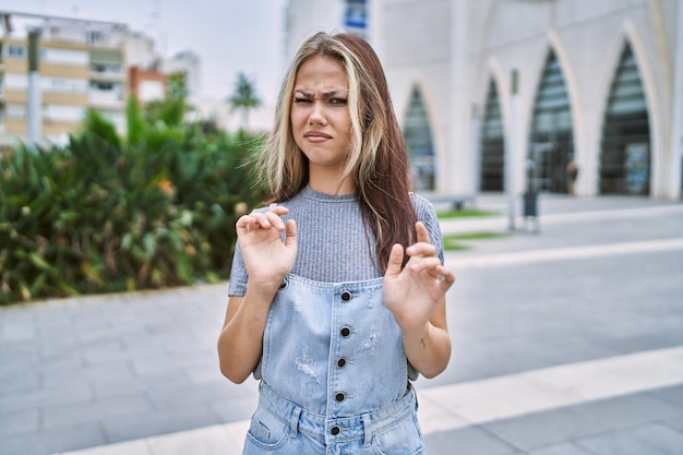 Free photo young caucasian woman outdoors disgusted expression, displeased and fearful doing disgust face because aversion reaction. with hands raised