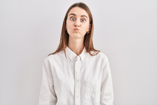 Young caucasian woman standing over isolated background puffing cheeks with funny face. mouth inflated with air, crazy expression.