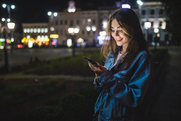 Young Caucasian woman texting cell phone in city at night