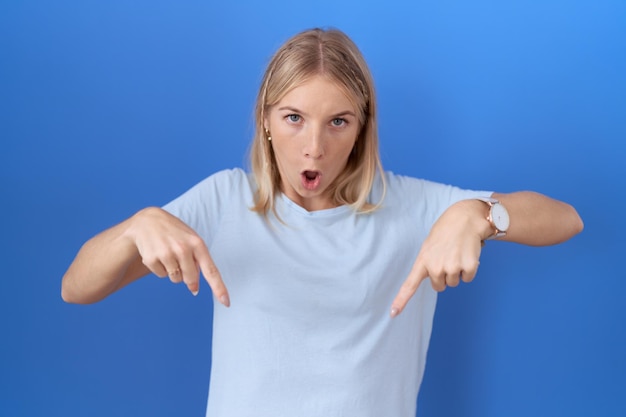 Free photo young caucasian woman wearing casual blue t shirt pointing down with fingers showing advertisement surprised face and open mouth