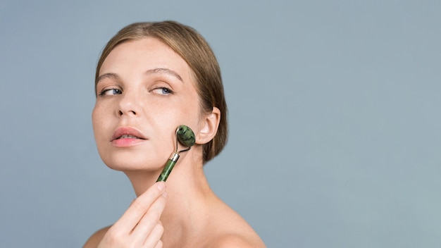 Free Photo a young caucasian woman with blue eyes doing a facial massage using a roller