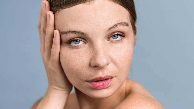 A young caucasian woman with blue eyes is looking into the camera and touching her face