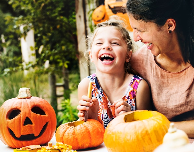 Free photo young cheerful girl carving pumpkins with her mom