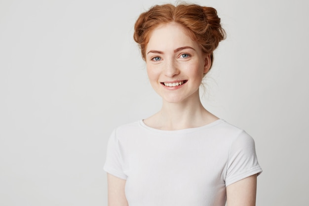 Young cheerful happy ginger girl with buns and freckles smiling .