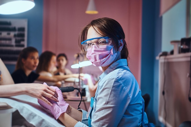 Young cheerful manicure master at her own workplace with client is working on woman's nails.