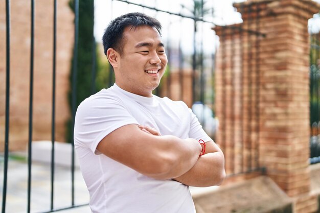 Young chinese man smiling confident standing with arms crossed gesture at street