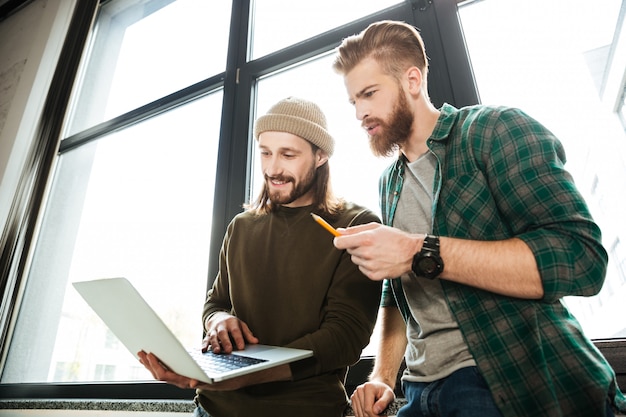 Free photo young concentrated men colleagues in office using laptop