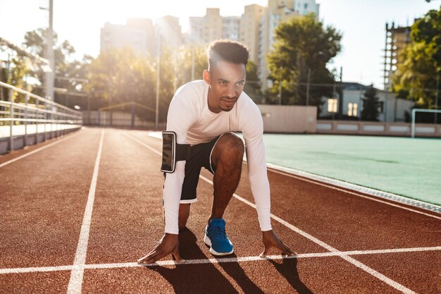 Young confident African American sportsman preparing for running on racetrack at city stadium