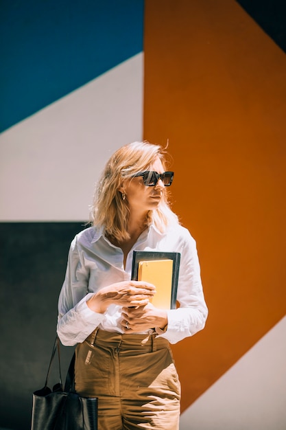 Young confident businesswoman holding diary in hand standing against colored wall