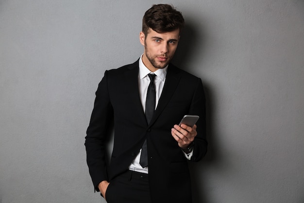 Free Photo young confident businnesman with hand in his pocket holding mobile phone, 