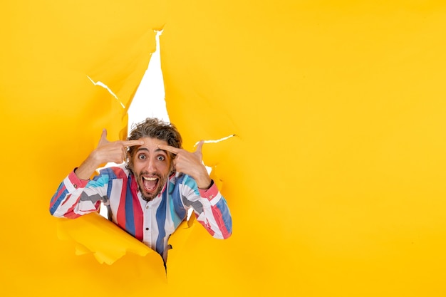 Free photo young confused bearded guy in a torn hole and free space in yellow paper