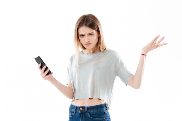 Young confused young woman holding mobile phone and shrugging shoulders