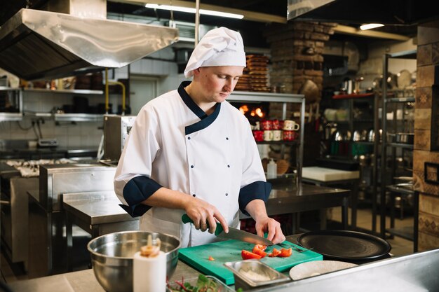 Young cook cutting tomato on board