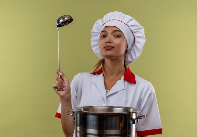  young cook female wearing chef uniform holding saucepan and ladle on isolated green wall