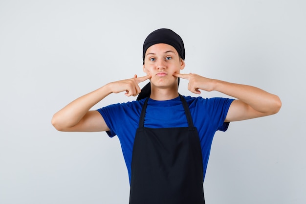 Free photo young cook in t-shirt, apron pressing fingers on dimples and looking bored , front view.