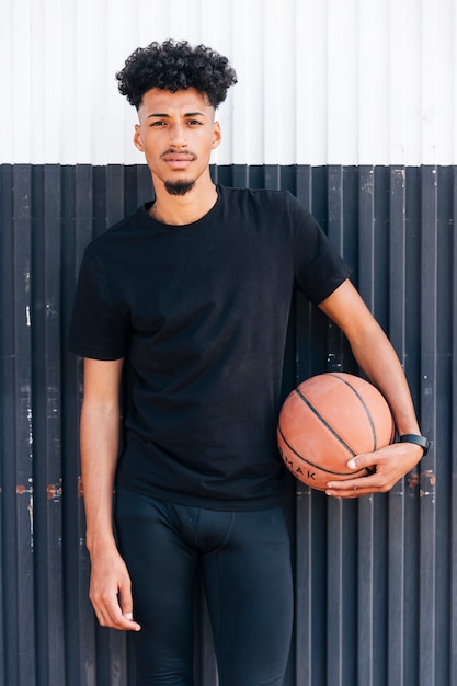 Young cool man standing against wall holding basketball 