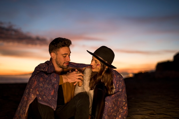 Young couple in blanket holding hands on sea shore