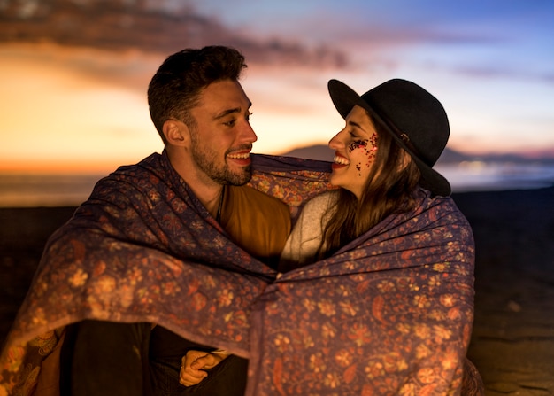 Free photo young couple in blanket laughing on sea shore