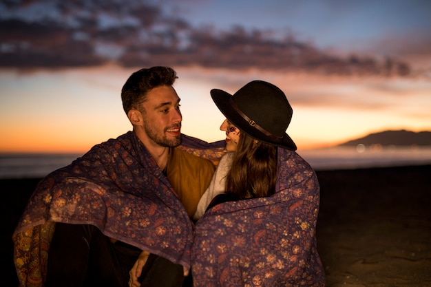 Free photo young couple in blanket smiling on sea shore