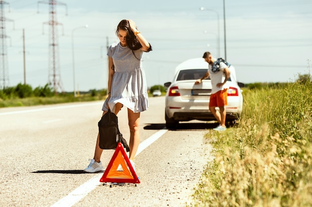 Free Photo the young couple broke down the car while traveling on the way to rest. they are trying to stop other drivers and ask for help or hitchhike