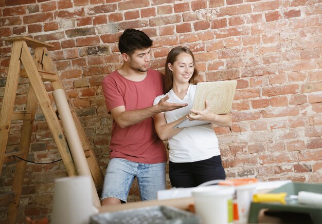 Young couple doing apartment repair together themselves. Married man and woman doing home makeover or renovation. Concept of relations, family, love. Choosing the design of the wall with notebook.