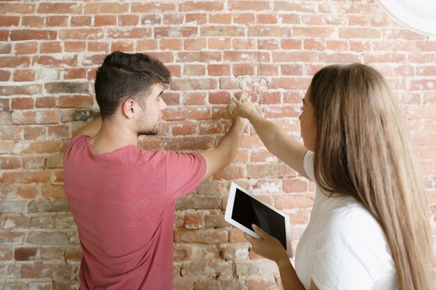 Young couple doing apartment repair together themselves. Married man and woman doing home makeover or renovation. Concept of relations, family, love. Measure and discuss the future design on the wall.