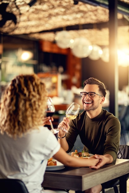 Young couple drinking wine and having fun during lunch in a bar Focus is on man