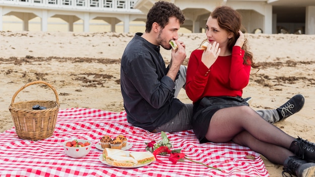 Young couple eating sandwiches on coverlet 