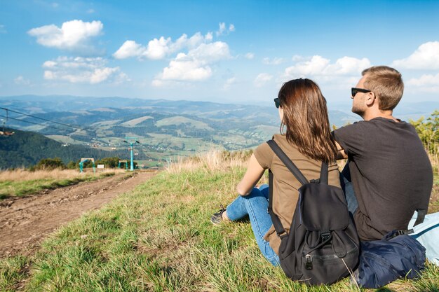 Young couple enjoying mountains landscape, sitting on hill