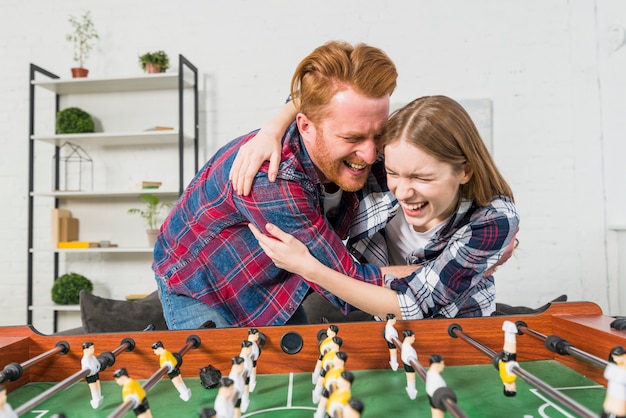 Young couple enjoying behind the table soccer game at home