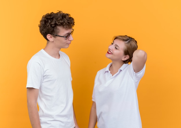 Free Photo young couple happy man and woman looking at each other smiling cheerfully standing over orange wall