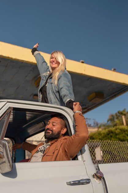 Young couple having fun on their car trip with woman in the back trunk