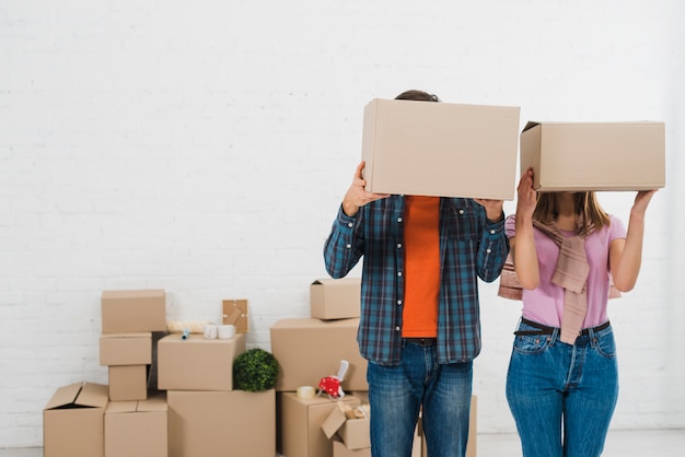 Free photo young couple hiding their faces with cardboard boxes in new house