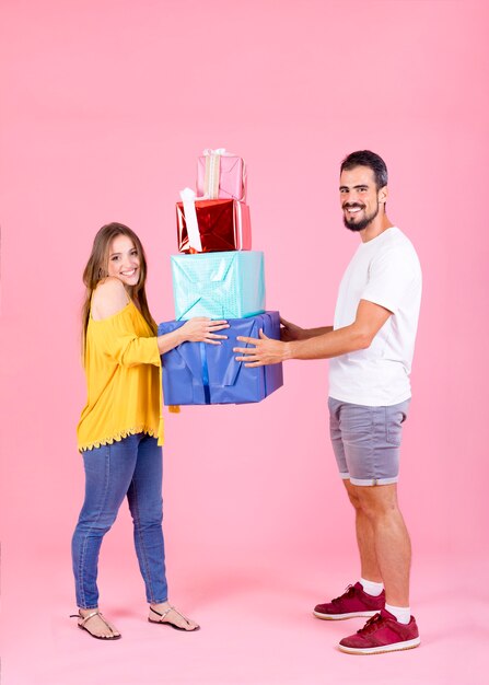 Young couple holding colorful gift boxes against pink backdrop