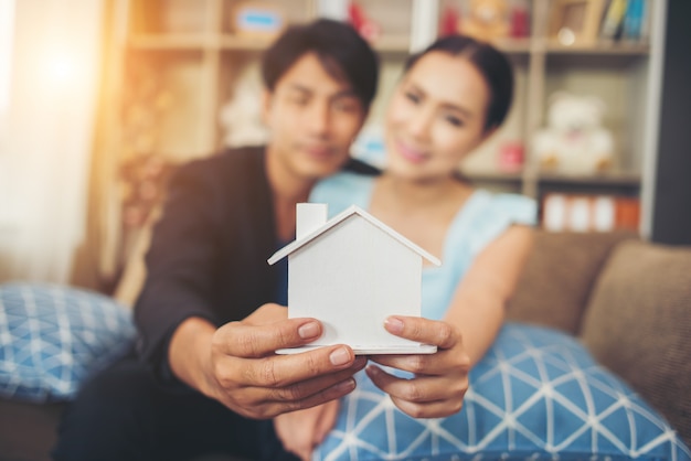 Young couple holding a white miniature house in living room