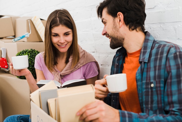 Young couple looking at books in the cardboard box holding coffee cups in hand