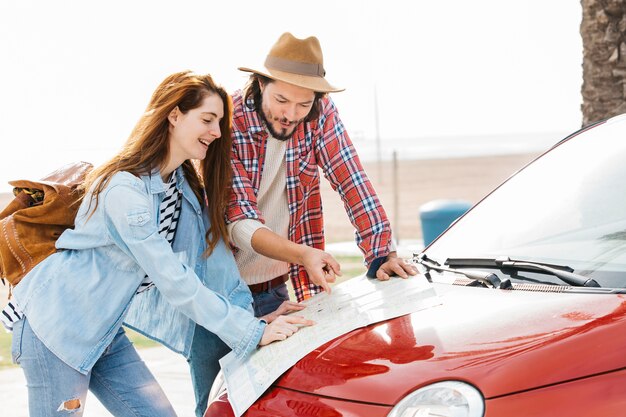 Young couple looking at road map on red car