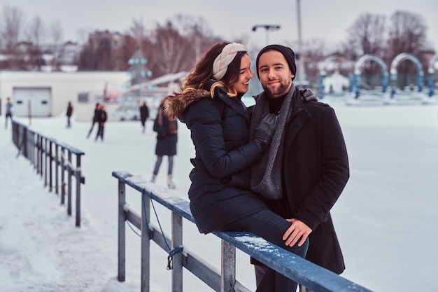 Young couple in love, date at the ice rink, a girl sitting on a guardrail and embracing with her boyfriend.