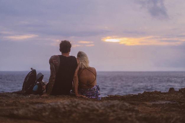 A young couple in love on a journey sits on the edge of a cliff and watches the sunset.